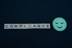 Compliance written in wooden letters next to smiley emoji.